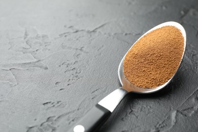 Photo of Spoon with instant coffee powder on dark textured table, closeup. Space for text