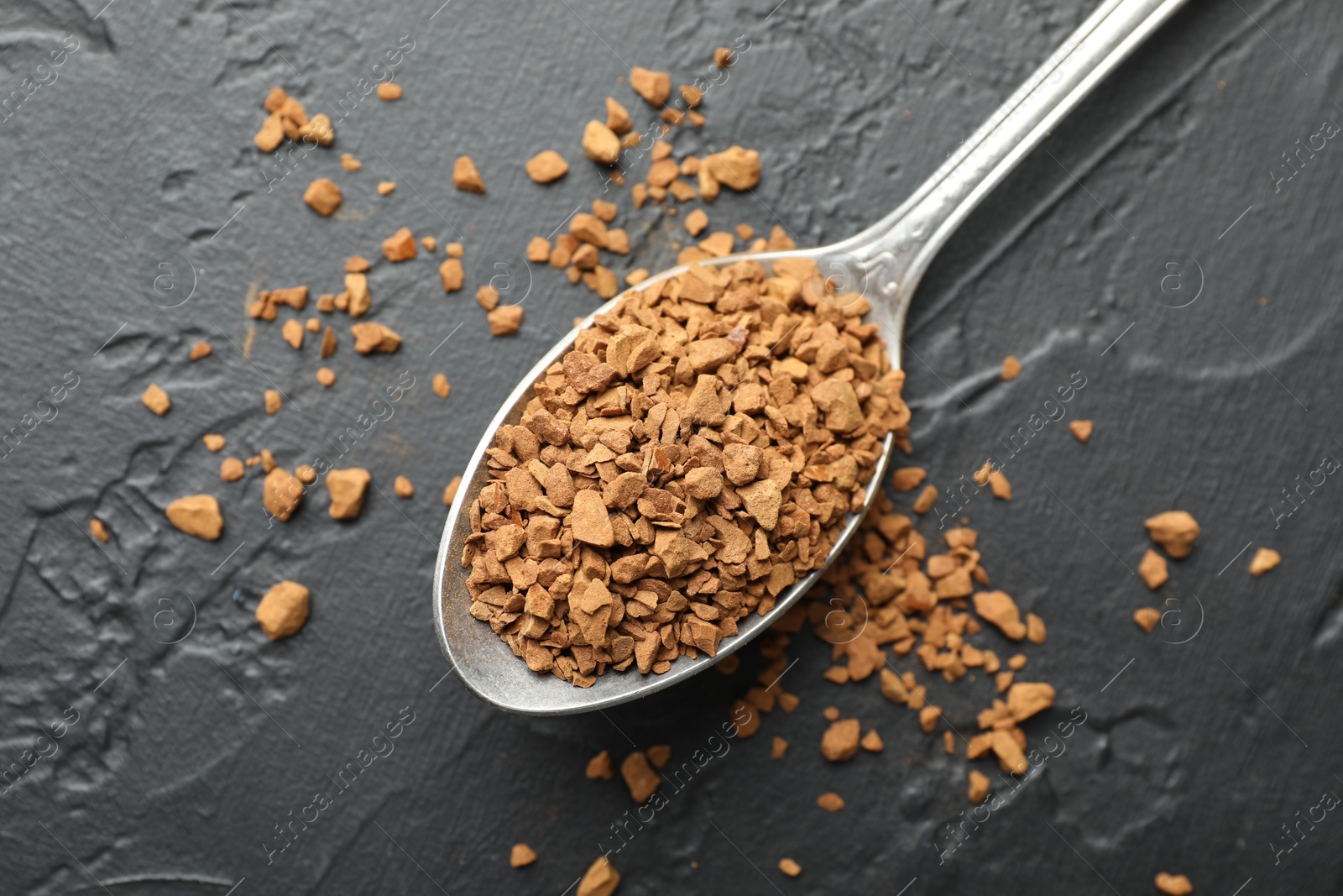 Photo of Spoon with granulated instant coffee on dark textured table, top view