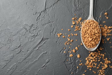 Photo of Spoon with granulated instant coffee on dark textured table, top view. Space for text