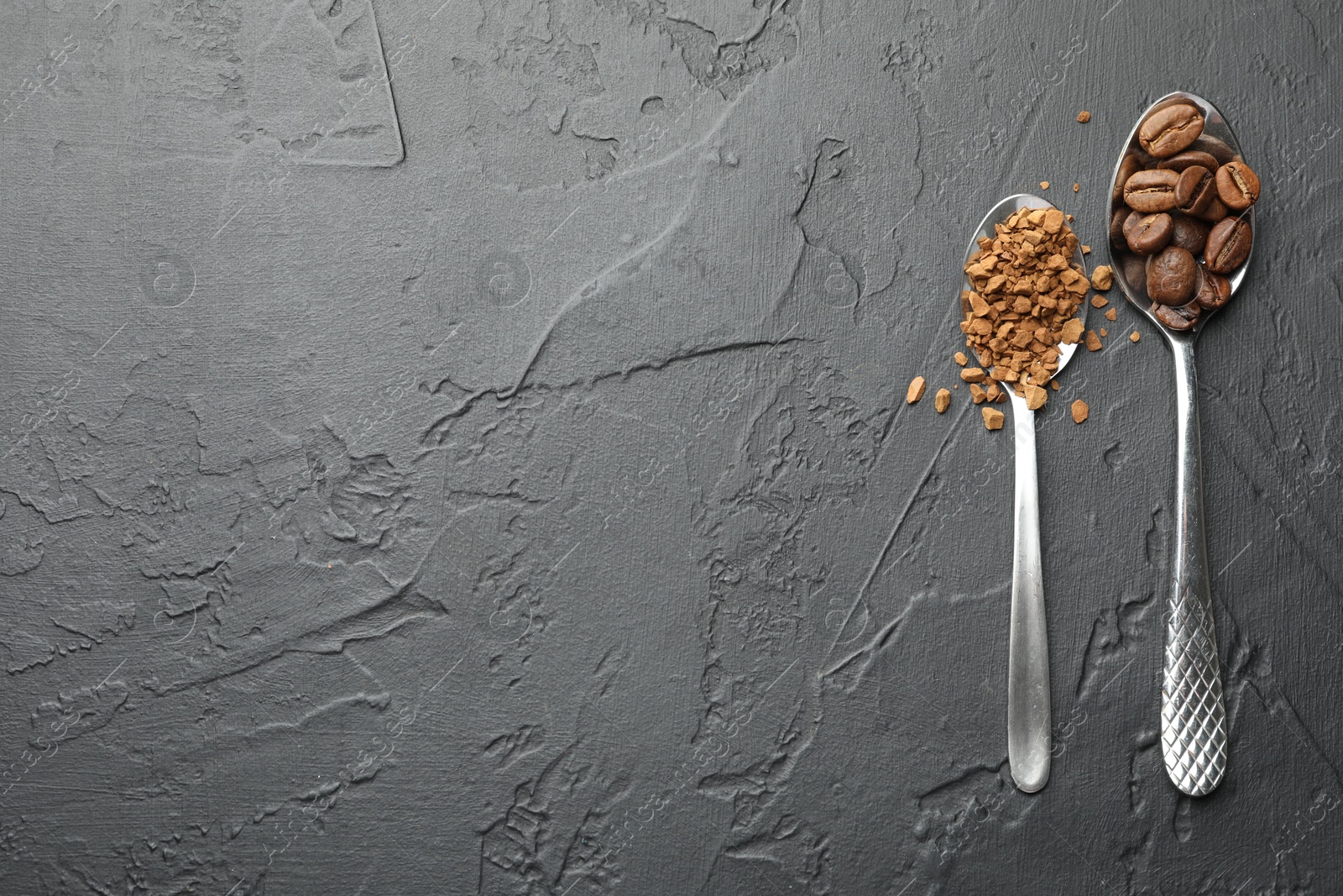 Photo of Spoons with granulated instant coffee and beans on dark textured table, flat lay. Space for text