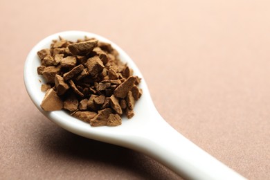 Photo of Spoon with granulated instant coffee on beige background, closeup