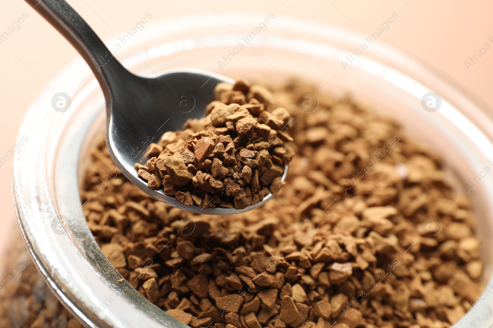 Photo of Taking granulated instant coffee from jar with spoon on beige background, closeup