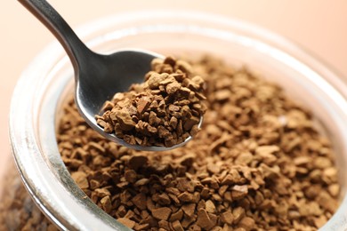 Photo of Taking granulated instant coffee from jar with spoon on beige background, closeup