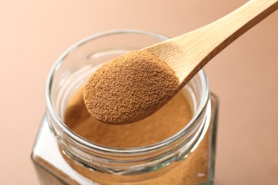 Photo of Spoon with instant coffee powder and jar on beige background, closeup