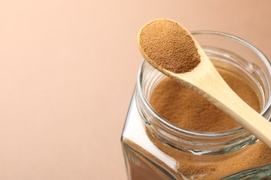 Photo of Spoon with instant coffee powder and jar on beige background, closeup. Space for text