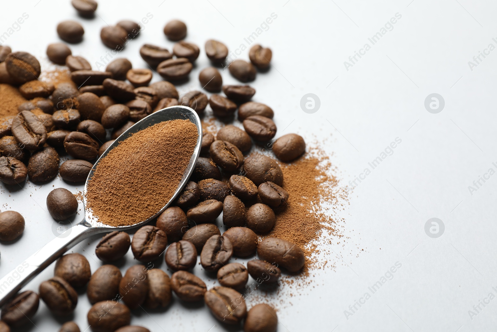 Photo of Spoon with instant coffee powder and beans on white background, closeup. Space for text