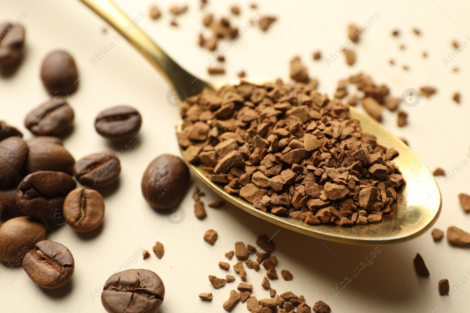 Photo of Spoon with granulated instant coffee and beans on beige background, closeup