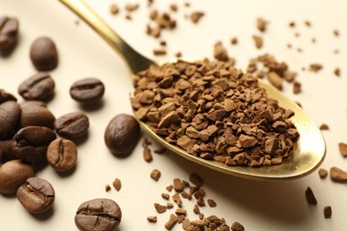 Photo of Spoon with granulated instant coffee and beans on beige background, closeup