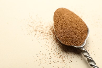Photo of Spoon with instant coffee powder on beige background, closeup. Space for text