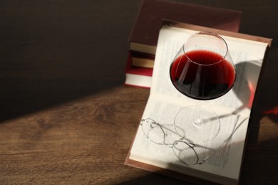 Photo of Glass of wine, books and glasses on wooden table. Space for text