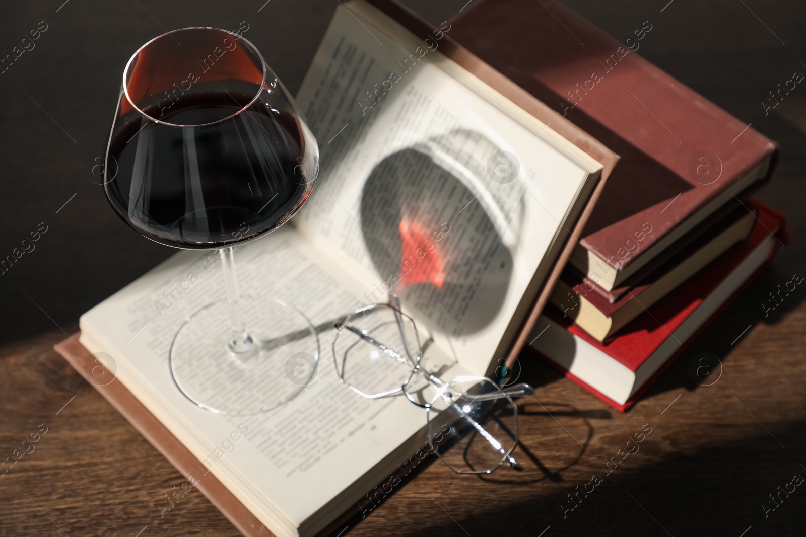 Photo of Glass of wine, books and glasses on wooden table