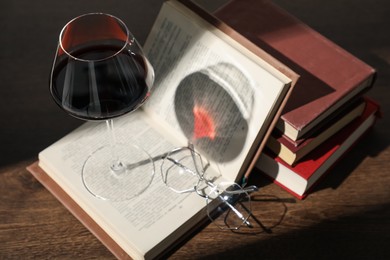 Photo of Glass of wine, books and glasses on wooden table