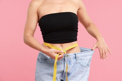 Photo of Fit woman with measuring tape wearing old jeans after weight loss on pink background, closeup