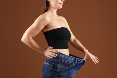 Photo of Fit woman wearing old jeans after weight loss on brown background, closeup