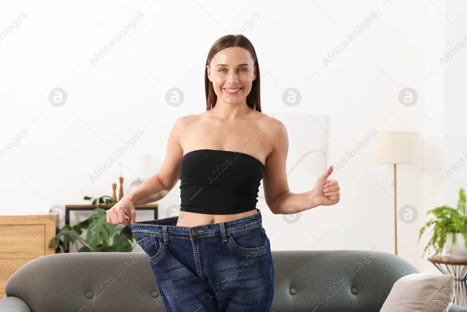 Photo of Fit woman wearing old jeans after weight loss and showing thumbs up at home