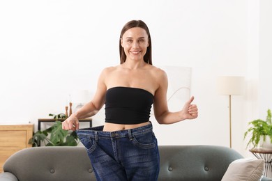 Photo of Fit woman wearing old jeans after weight loss and showing thumbs up at home