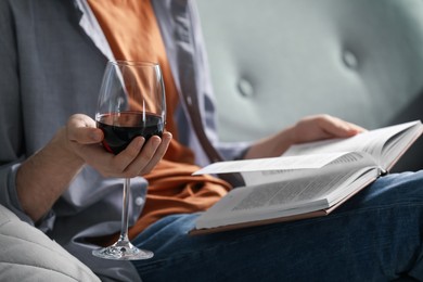 Photo of Woman with glass of wine reading book on sofa at home, closeup