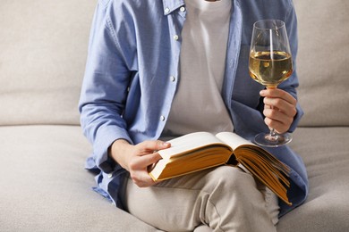 Photo of Woman with glass of wine reading book on sofa at home, closeup