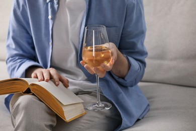 Photo of Woman with glass of wine reading book on sofa at home, closeup