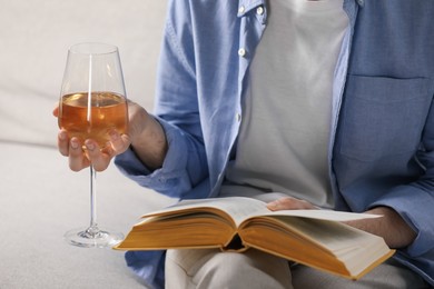 Photo of Woman with glass of wine reading book on sofa at home, closeup