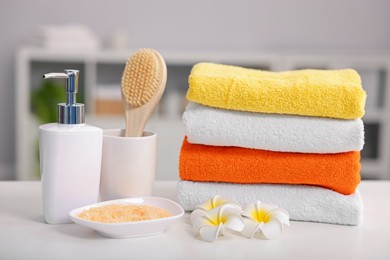 Photo of Stack of colorful towels, bath accessories and plumeria flowers on white table indoors