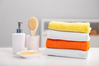 Photo of Stack of colorful towels, sea salt, liquid soap and brush on white table indoors