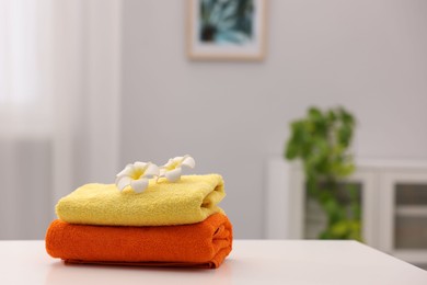 Photo of Stack of colorful towels and plumeria flowers on white table indoors, space for text