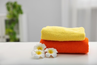 Photo of Stack of colorful towels and plumeria flowers on white table indoors, closeup. Space for text