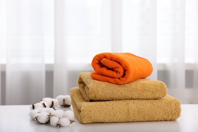 Photo of Stack of colorful towels and cotton flowers on white table indoors