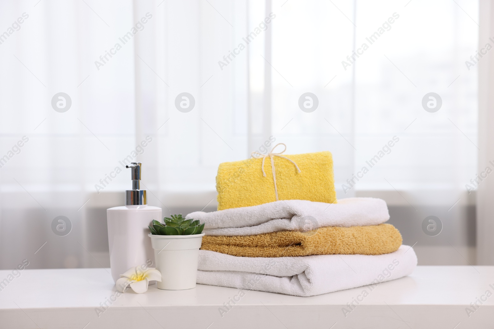 Stack of colorful towels, liquid soap and floral decor on white table indoors, Photo of Stack of colorful towels, liquid soap and floral decor on white table indoors,