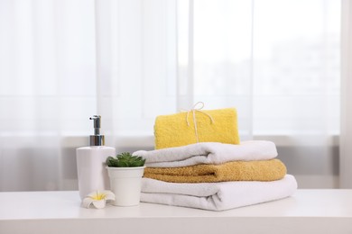 Photo of Stack of colorful towels, liquid soap and floral decor on white table indoors,