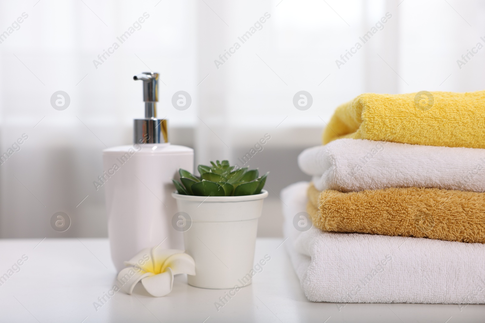 Stack of colorful towels, liquid soap and floral decor on white table indoors, closeup Photo of Stack of colorful towels, liquid soap and floral decor on white table indoors, closeup