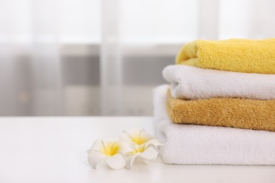 Photo of Stack of colorful towels and plumeria flowers on white table indoors, closeup. Space for text
