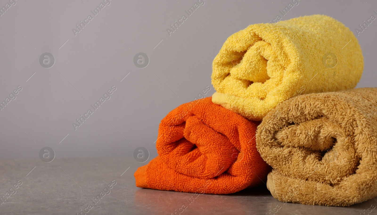 Rolled colorful towels on grey table, closeup. Space for text Photo of Rolled colorful towels on grey table, closeup. Space for text