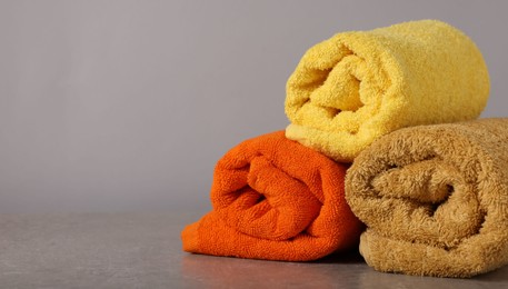 Photo of Rolled colorful towels on grey table, closeup. Space for text