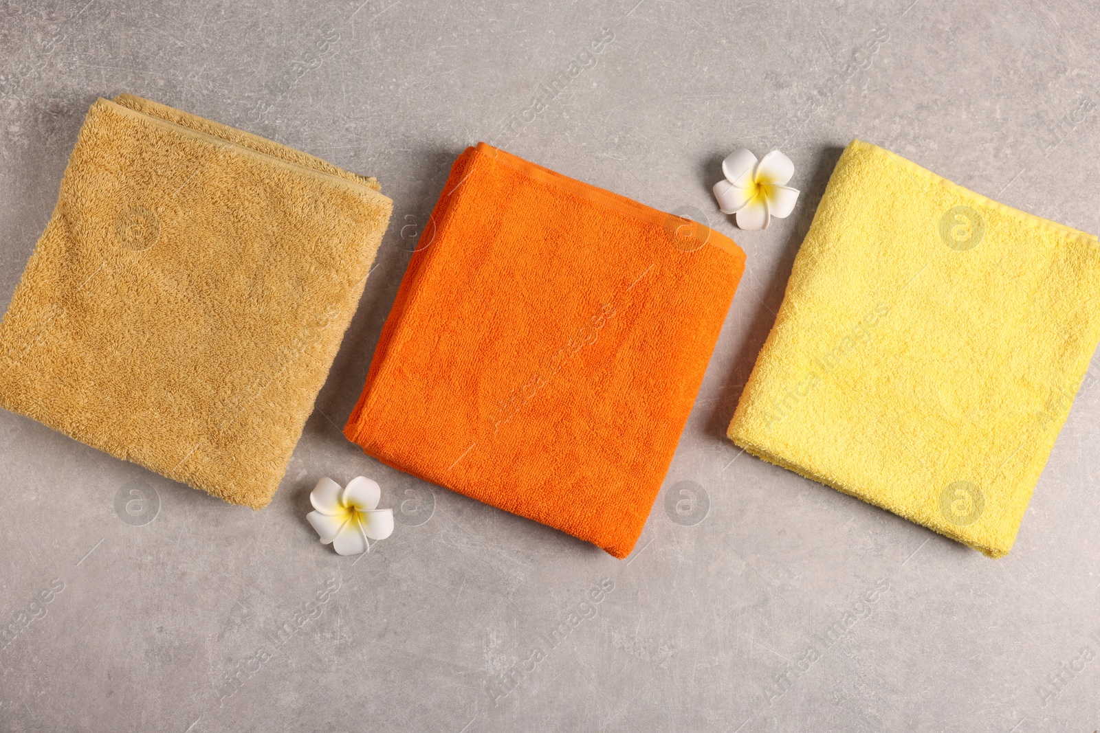 Colorful towels and plumeria flowers on grey table, flat lay Photo of Colorful towels and plumeria flowers on grey table, flat lay
