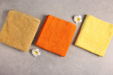 Photo of Colorful towels and plumeria flowers on grey table, flat lay
