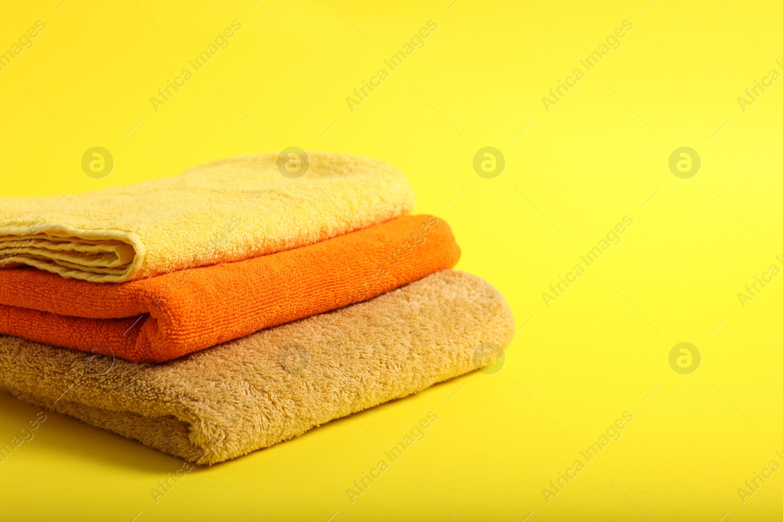 Stack of colorful towels on yellow background, closeup. Space for text Photo of Stack of colorful towels on yellow background, closeup. Space for text