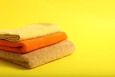 Photo of Stack of colorful towels on yellow background, closeup. Space for text