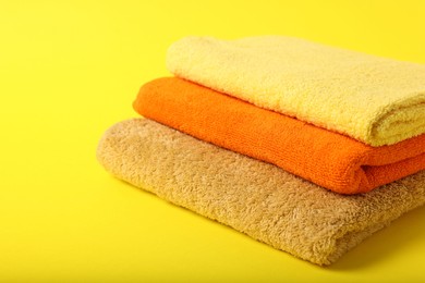 Photo of Stack of colorful towels on yellow background, closeup. Space for text