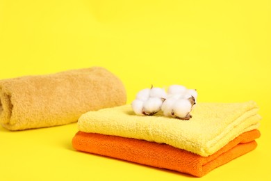 Photo of Colorful towels and cotton flowers on yellow background, closeup