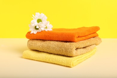 Photo of Stack of colorful towels and chrysanthemum flowers on beige table against yellow background, closeup
