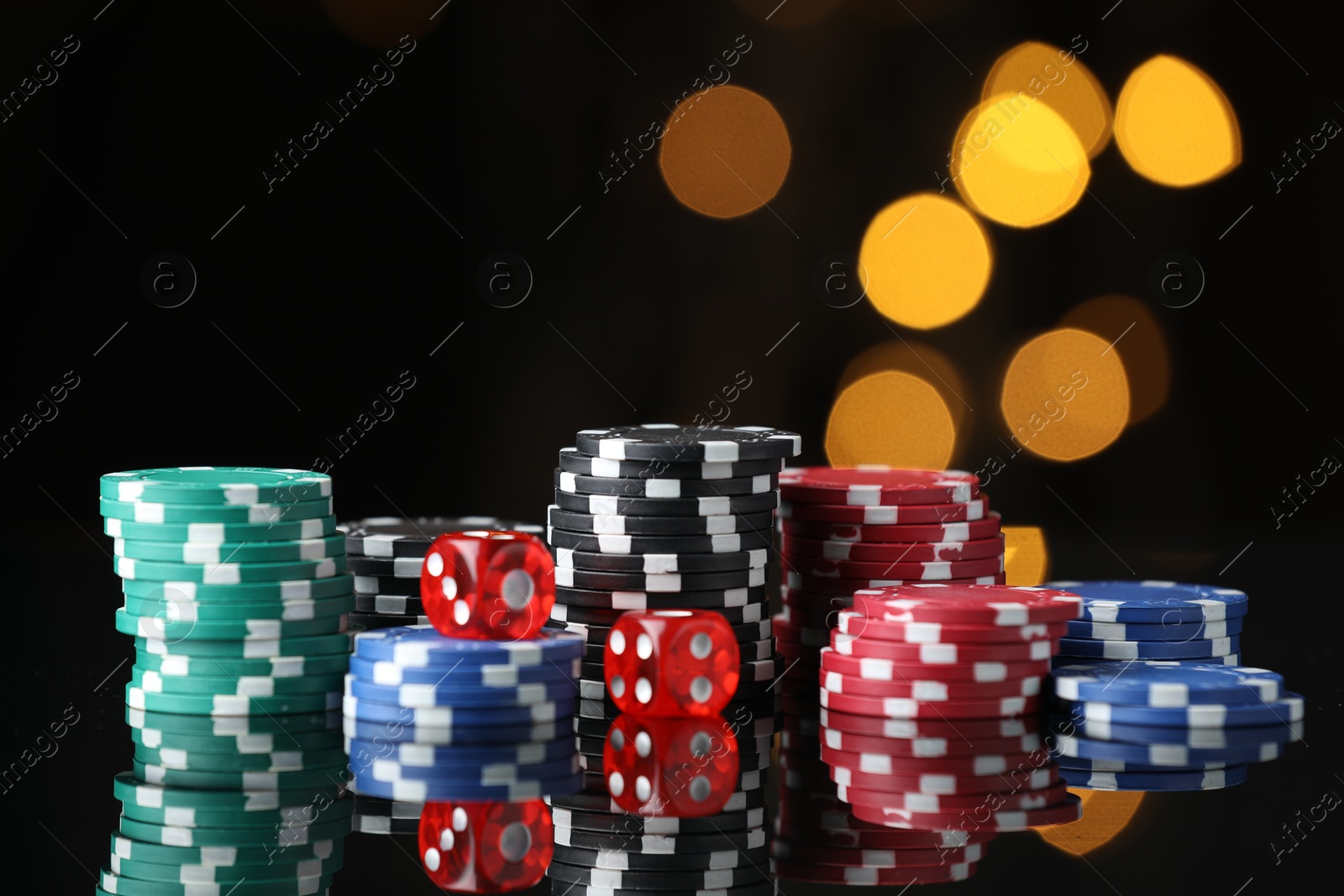 Photo of Casino chips and dice on mirror surface against blurred lights, closeup