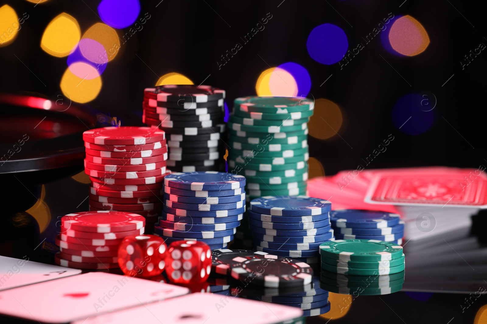 Casino chips, playing cards and dice on mirror surface against blurred lights, closeup Photo of Casino chips, playing cards and dice on mirror surface against blurred lights, closeup