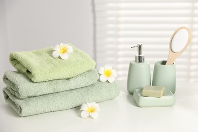 Photo of Fresh terry towels, cosmetic products and plumeria flowers on white table in bathroom