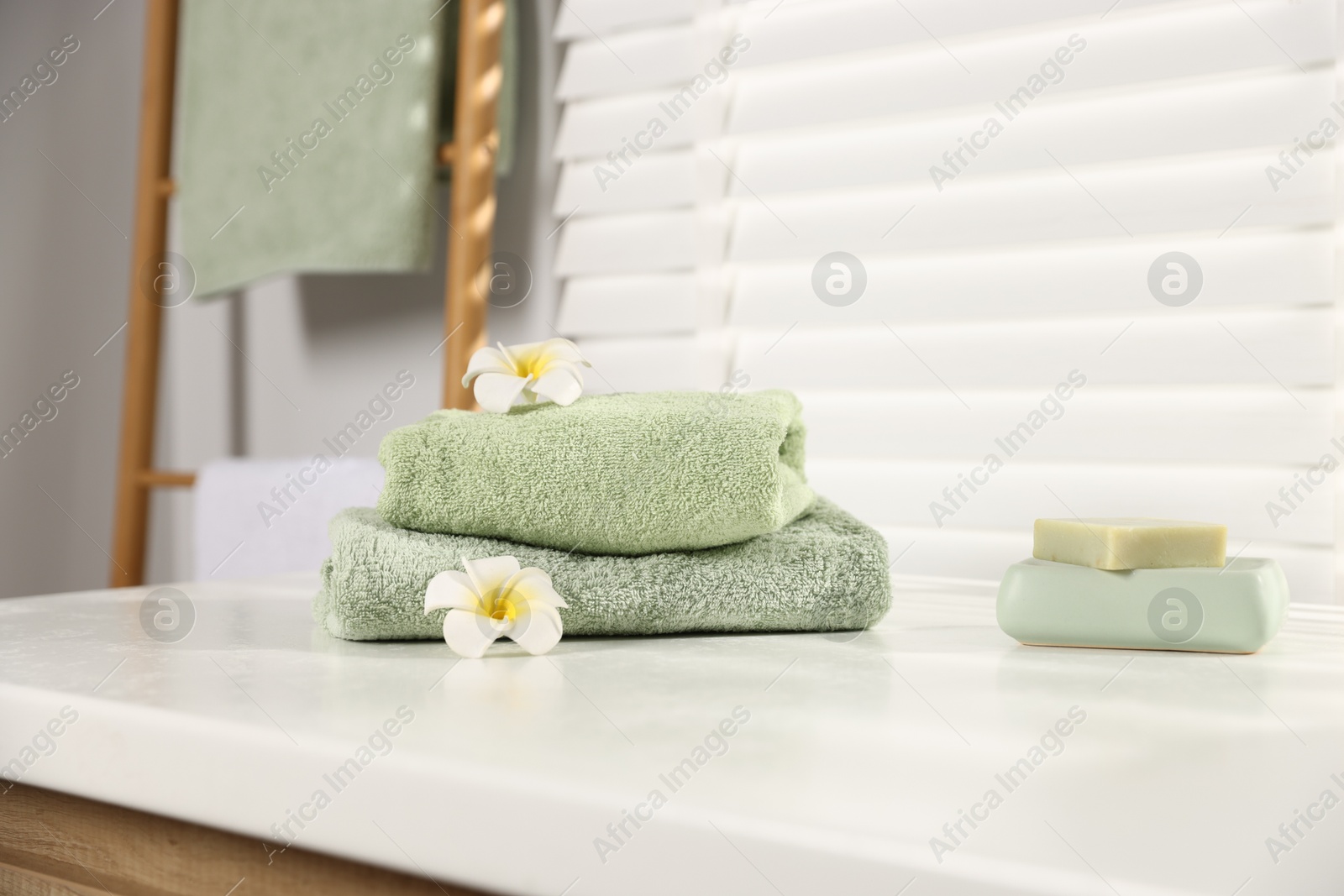 Fresh terry towels, soap and plumeria flowers on white table in bathroom Photo of Fresh terry towels, soap and plumeria flowers on white table in bathroom