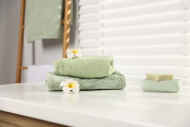 Photo of Fresh terry towels, soap and plumeria flowers on white table in bathroom