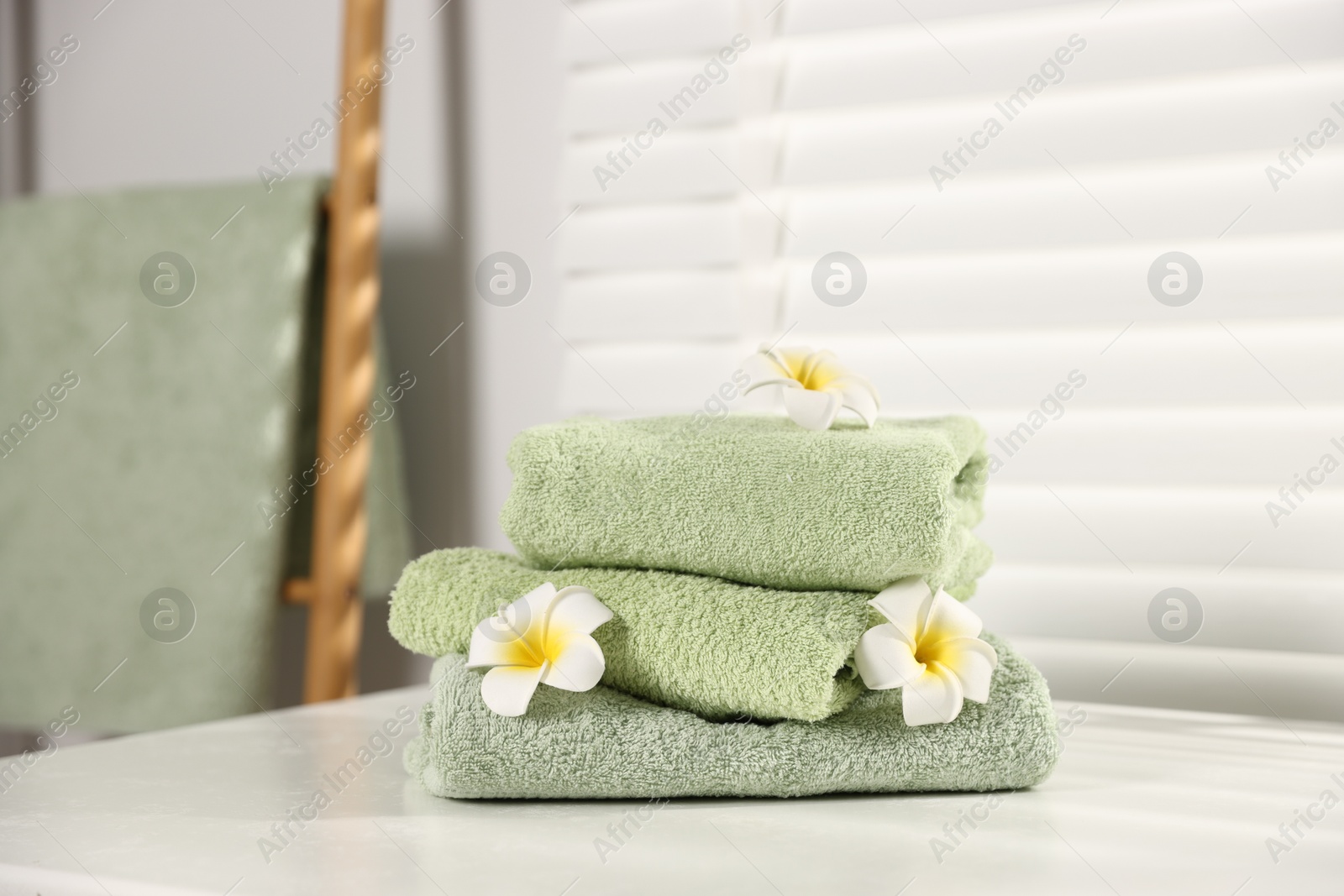 Fresh terry towels and plumeria flowers on white table in bathroom Photo of Fresh terry towels and plumeria flowers on white table in bathroom
