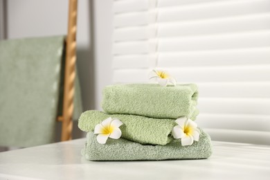 Photo of Fresh terry towels and plumeria flowers on white table in bathroom