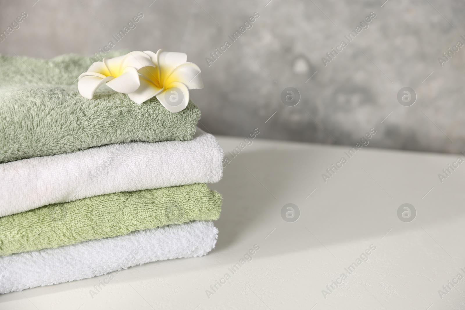 Fresh terry towels and plumeria flowers on white table, closeup. Space for text Photo of Fresh terry towels and plumeria flowers on white table, closeup. Space for text